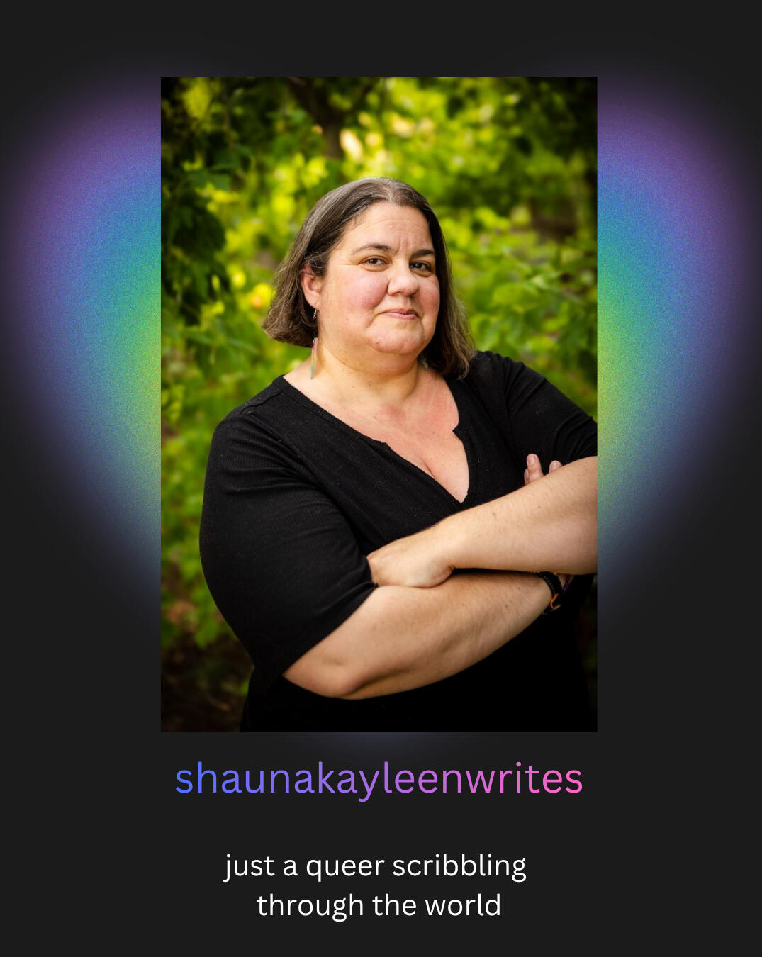 Shauna Brock, a white woman with brown and gray hair stands with her arms crossed in front of a background of trees. She wears a black shirt and multi-colored earrings.